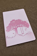 Pink journal with tree and bench design on a brown textured surface